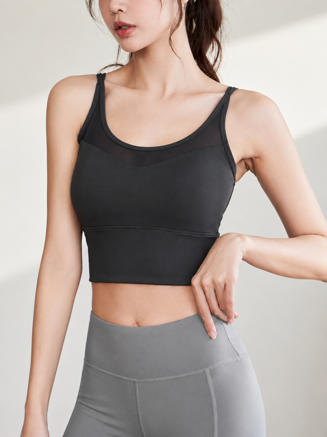 Person wearing a black sports bra and gray leggings on a plain background
