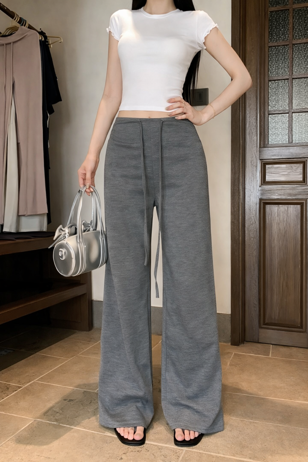Person wearing a white top and gray wide-leg pants holding a silver handbag indoors.