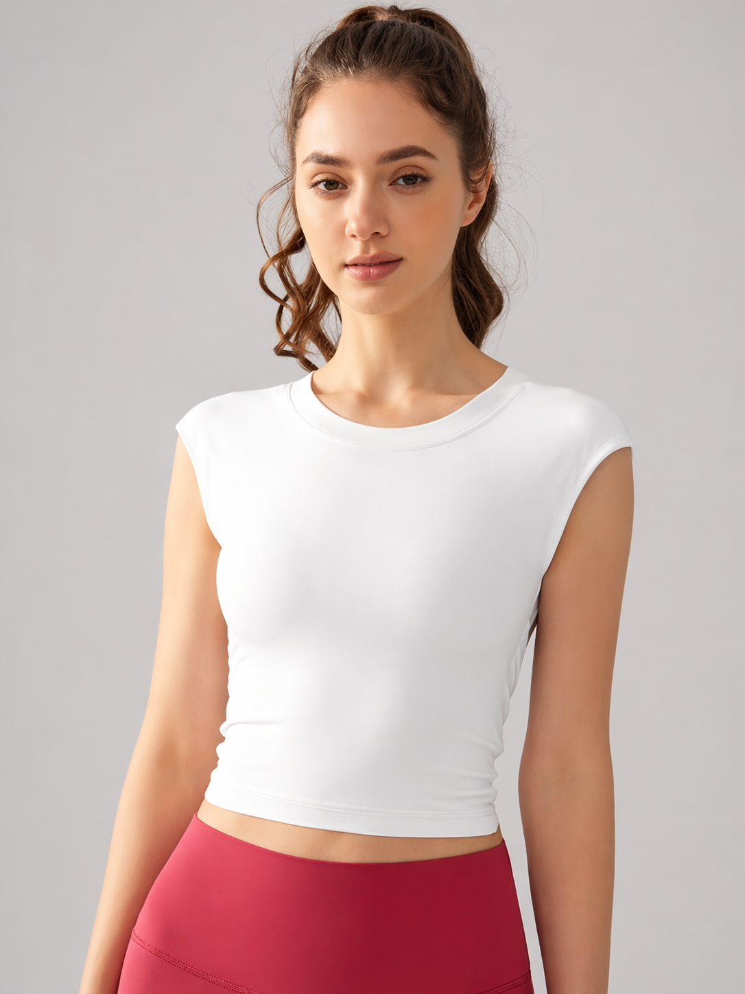 Woman wearing a white sleeveless top and red leggings against a gray background