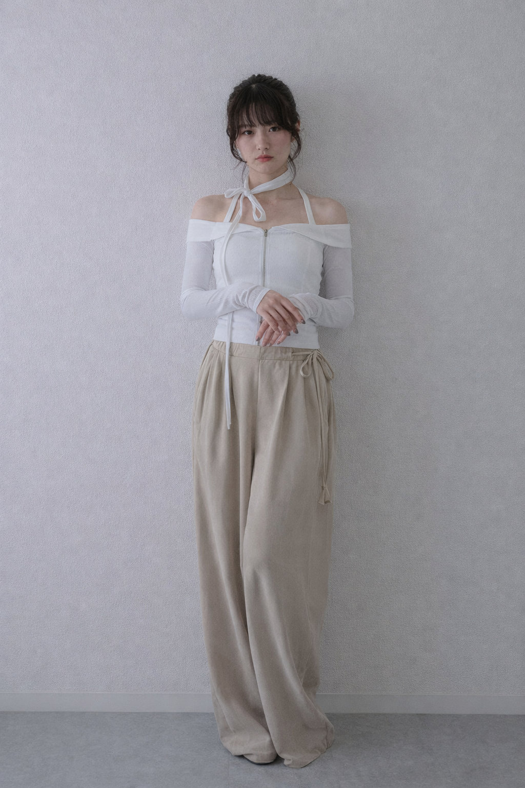Woman wearing a white off-shoulder top and beige pants against a plain background