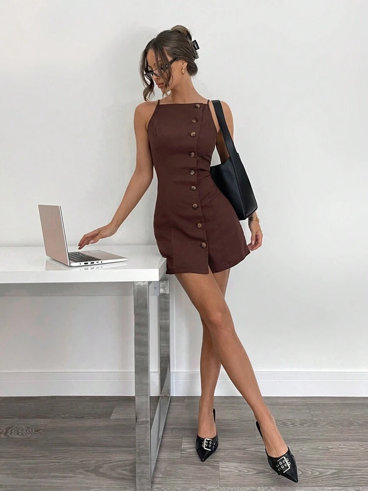 Woman in a brown dress standing next to a desk with a laptop, wearing black heels.